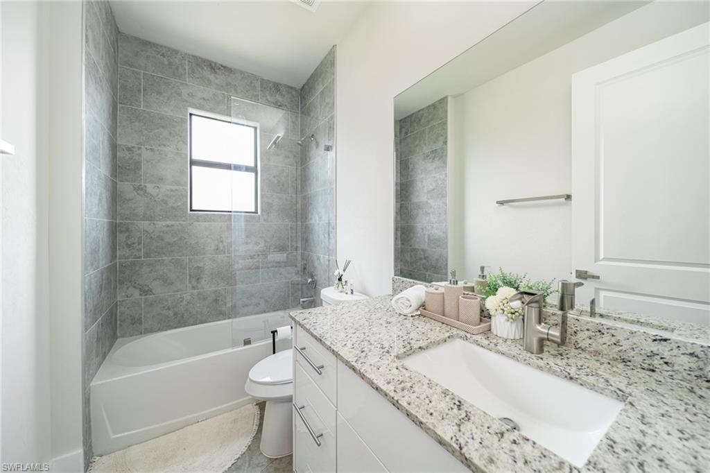 Contemporary bathroom featuring a spacious white tub with a tiled shower surround, a window providing natural light, a vanity with a white countertop and integrated sink, and white cabinetry