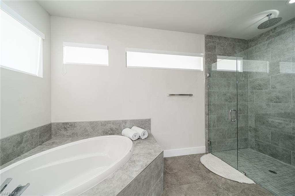 Contemporary bathroom featuring a freestanding oval tub, a frameless glass shower enclosure, a rainfall showerhead, and light gray tile flooring