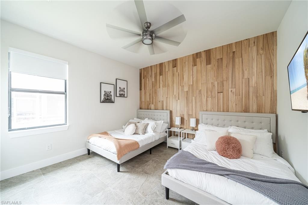 Spacious room featuring a wood-panel accent wall, contemporary ceiling fan, and large window with roller shades