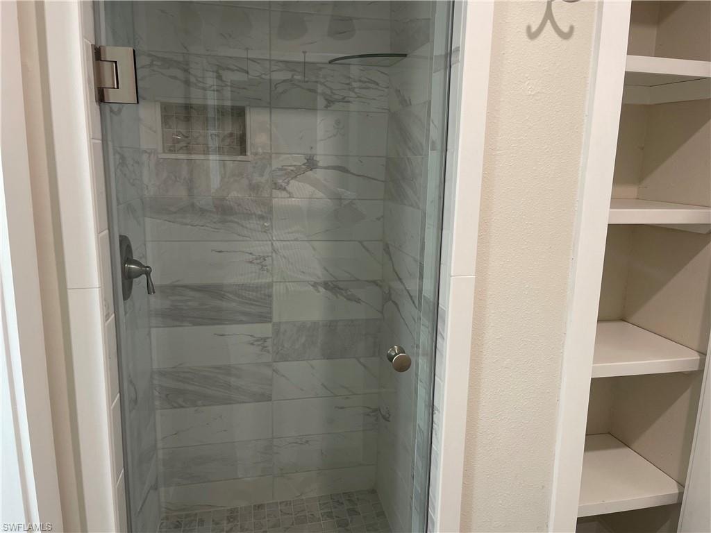 Glass-enclosed shower featuring large format tile with a subtle veined pattern, a built-in shower niche, and a mosaic tile floor