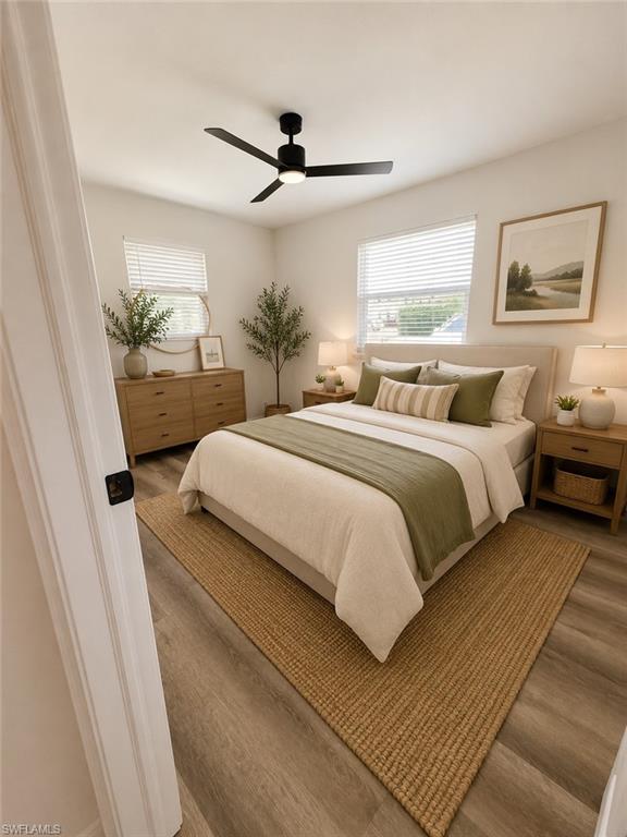 Bedroom featuring light wood-finish flooring, white walls, two windows with blinds, and a black ceiling fan with integrated lighting