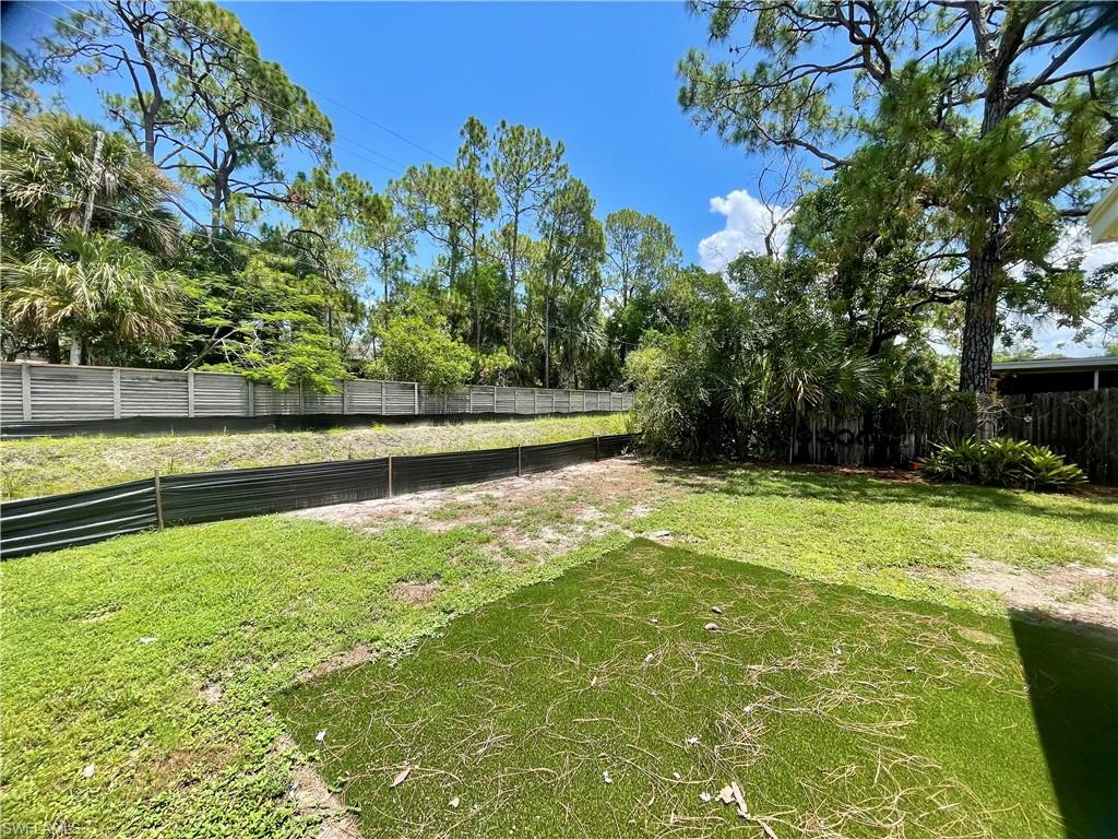 Spacious backyard featuring a section of artificial turf, natural grass, mature trees, and a privacy fence