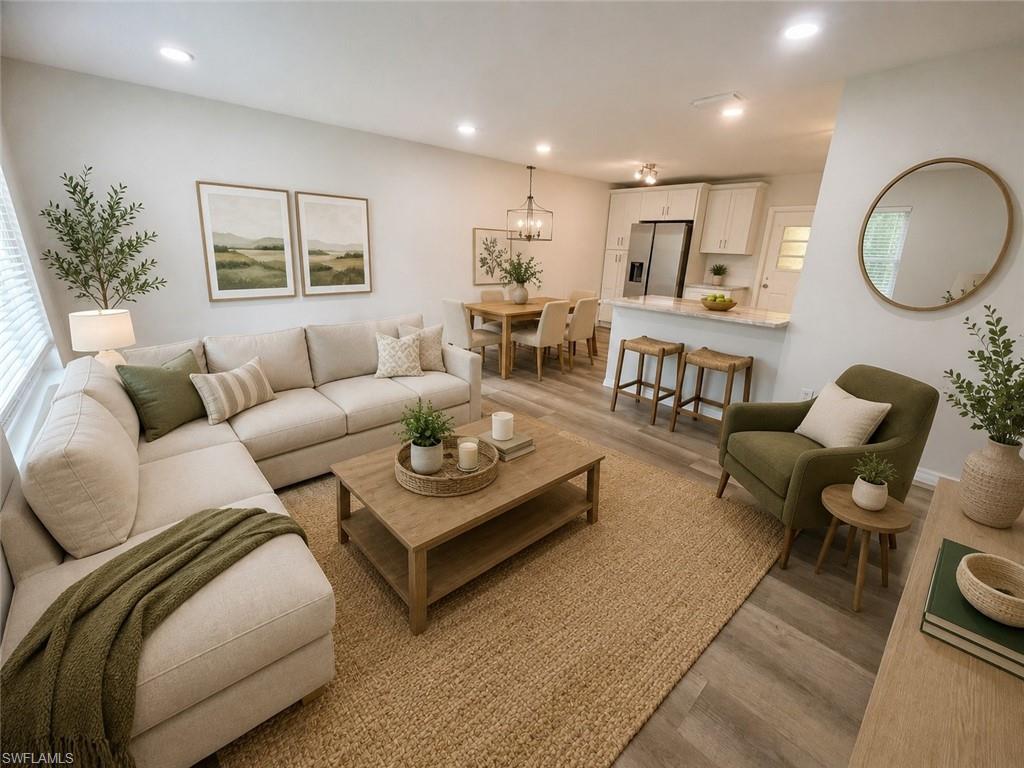 Open-concept living space featuring wood-finish flooring, recessed lighting, a kitchen with white cabinetry, a central island with a countertop, and a dining area with a chandelier