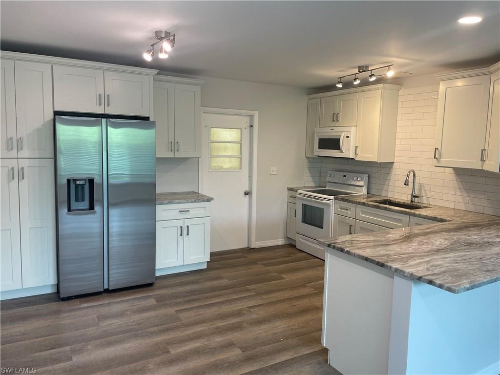 Bright kitchen featuring white shaker cabinetry, stainless steel appliances, wood-finish flooring, a subway tile backsplash, and a large counter space