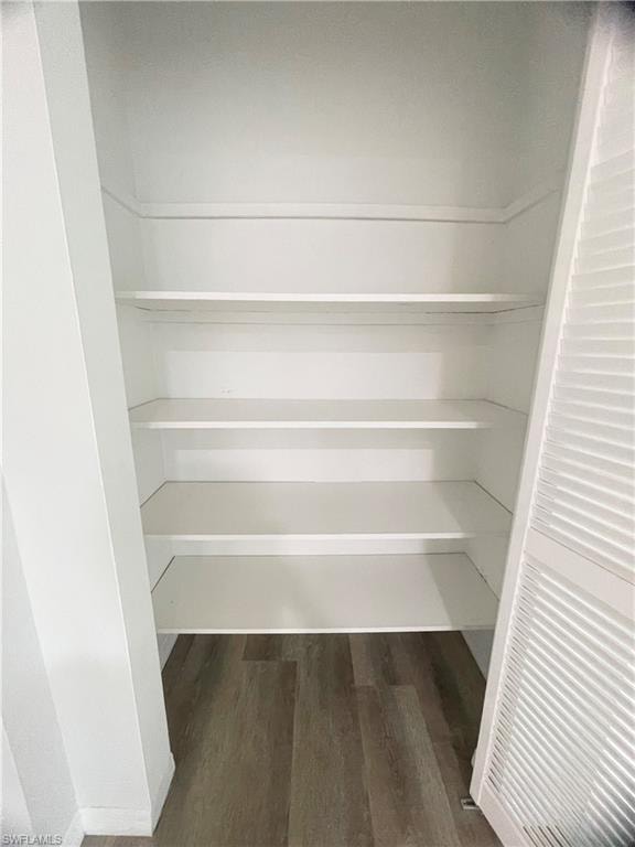 Built-in shelving unit with five white shelves, louvered bi-fold doors, and wood-finish flooring