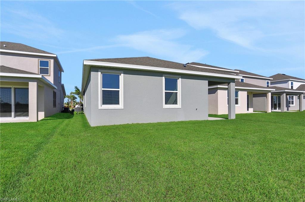 Rear view of house featuring a lawn, a patio area, stucco siding, and roof with shingles