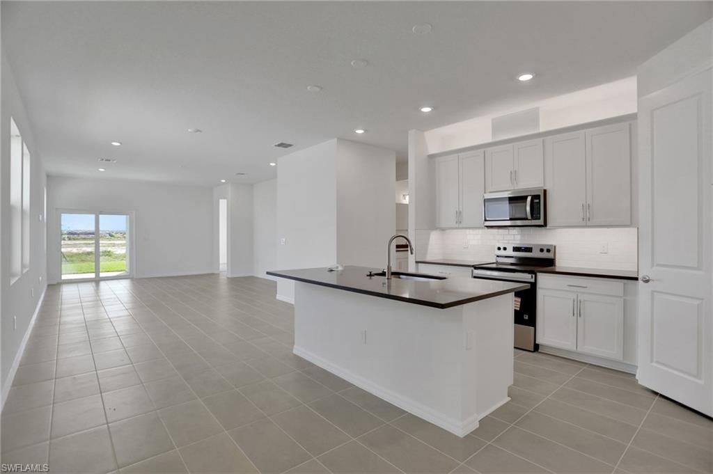 Kitchen featuring stainless steel appliances, dark countertops, a kitchen island with sink, white cabinetry, and recessed lighting