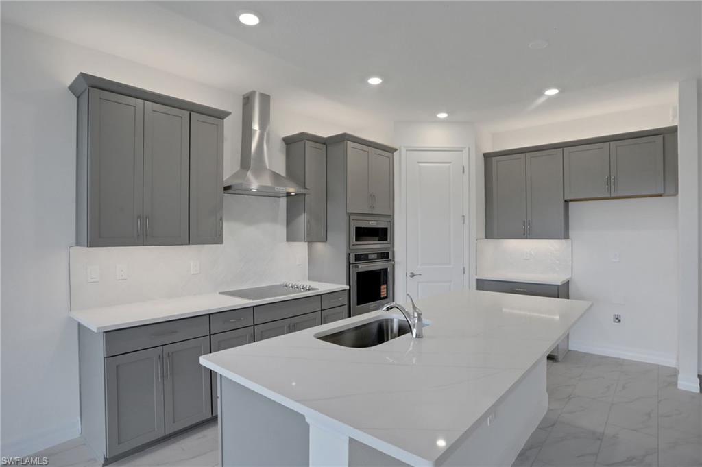 Kitchen featuring light stone countertops, an island with sink, gray cabinetry, recessed lighting, and stainless steel appliances