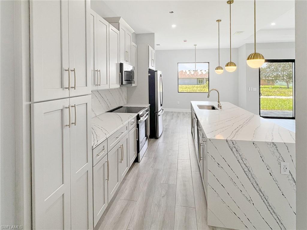 Kitchen featuring stainless steel appliances, light stone counters, light wood-type flooring, pendant lighting, and white cabinets