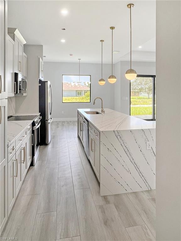 Kitchen featuring stainless steel appliances, light stone countertops, pendant lighting, and white cabinetry