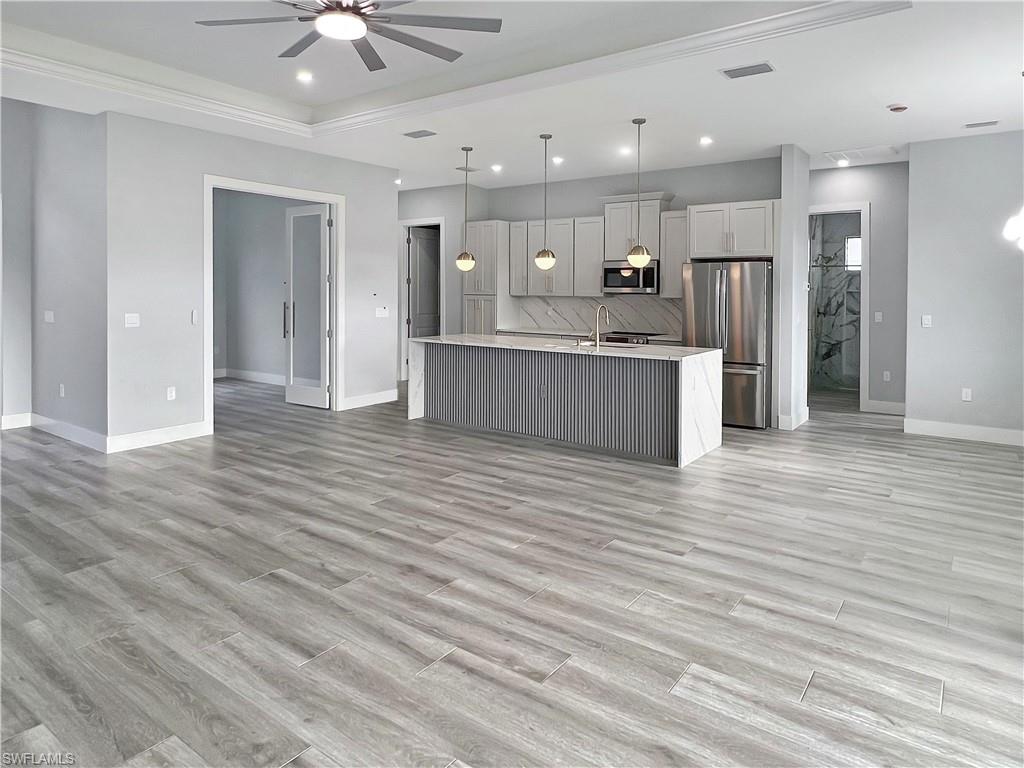 Kitchen featuring open floor plan, stainless steel appliances, a kitchen island with sink, hanging light fixtures, and a ceiling fan