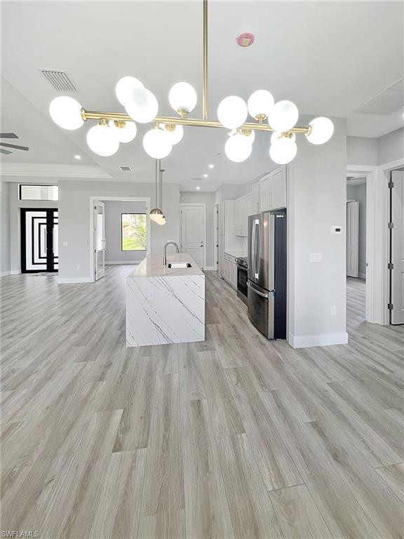 Kitchen featuring open floor plan, hanging light fixtures, stainless steel appliances, white cabinets, and a kitchen island with sink