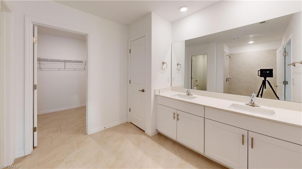 Dual vanity with white cabinetry and integrated sinks, oversized wall mirror, and tile flooring