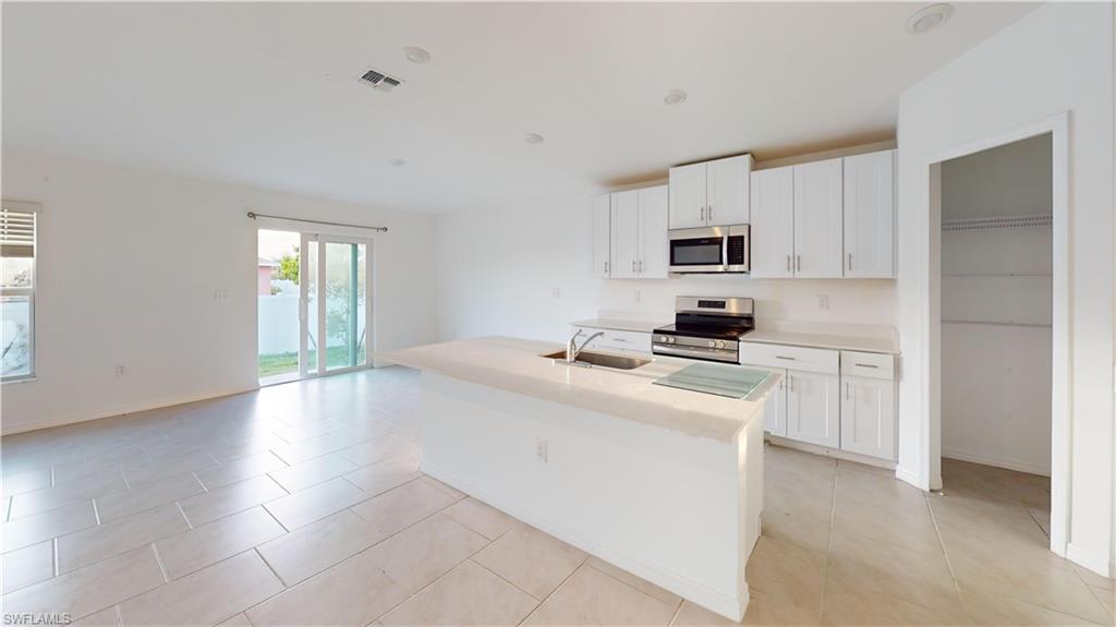 Open-concept kitchen and living area featuring a large center island with an undermount sink, white cabinetry, stainless steel appliances, and light-toned tile flooring