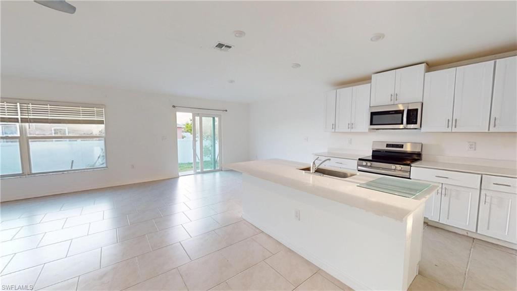 Open-concept living space featuring a kitchen island with sink, stainless steel appliances, white cabinetry, tile flooring, and sliding glass doors to the exterior