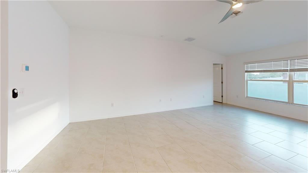 Spacious interior room featuring light-toned tile flooring, large windows with horizontal blinds, a modern ceiling fan with integrated lighting, and neutral wall finishes