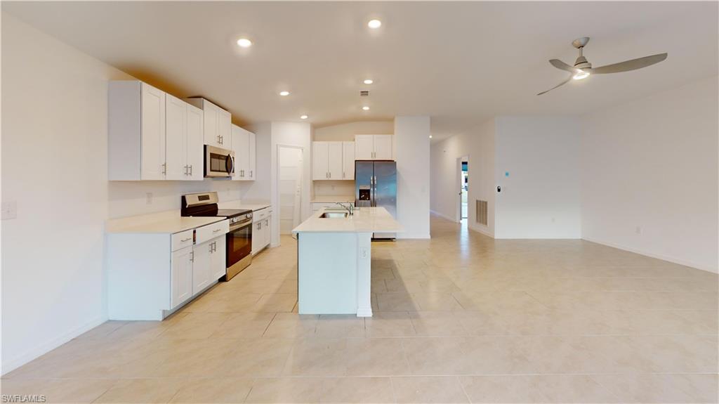 Open-concept living area featuring a kitchen island with sink, stainless steel appliances, white cabinetry, recessed lighting, and a ceiling fan
