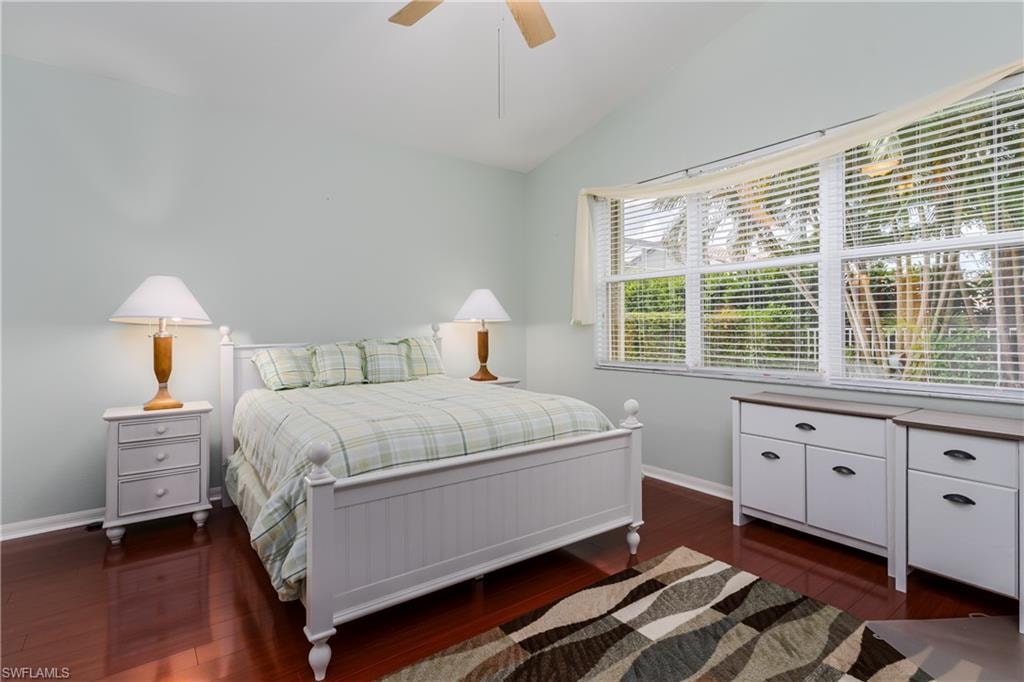 Vaulted ceiling, wood-finish flooring, multiple windows, ceiling fan, and light-toned walls