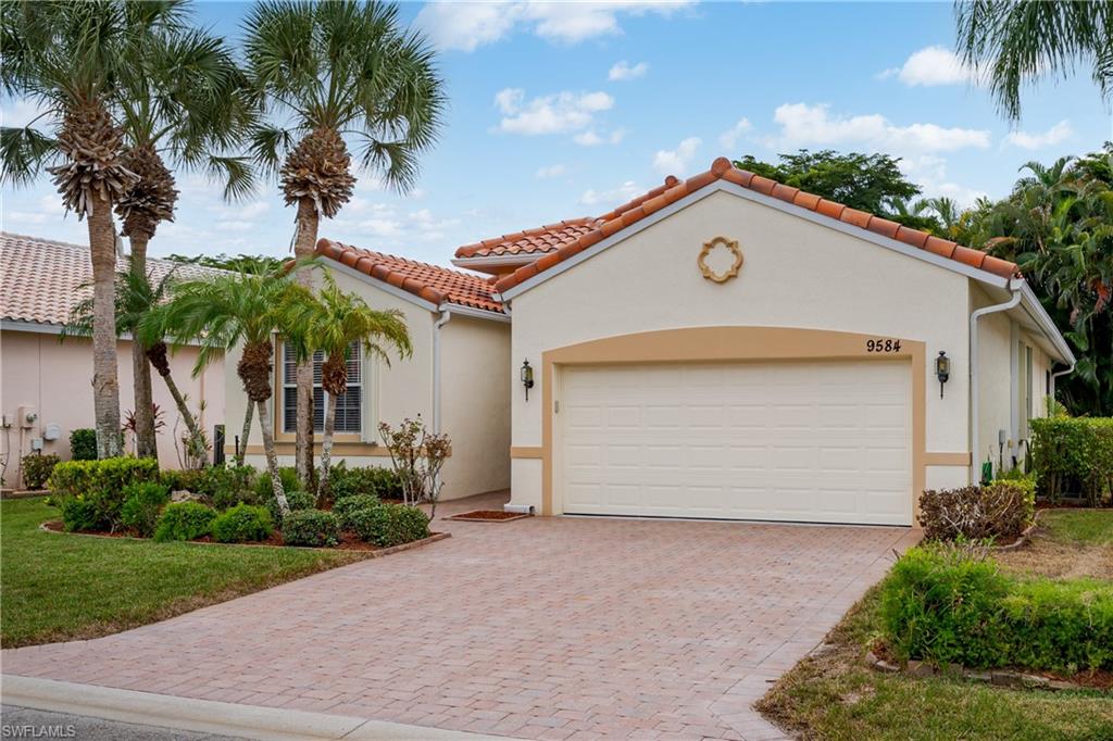 Mediterranean-inspired architecture with a barrel tile roof, stucco exterior, integrated two-car garage, paver driveway, and established tropical landscaping