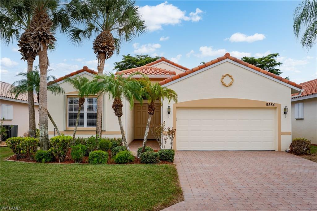 Stucco exterior with a terracotta tile roof, paver driveway, attached garage, and mature landscaping