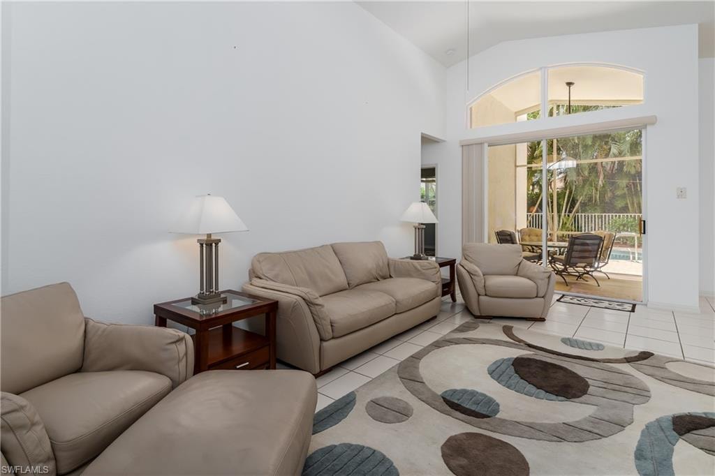 Vaulted ceiling, ceramic tile flooring, and sliding glass doors with an arched transom window opening to a screened patio with a pool