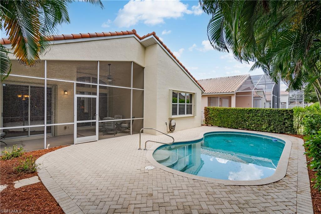 Curved swimming pool with paver surround, screened patio with sliding glass doors, and mature landscaping