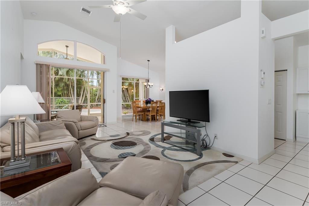 Vaulted ceilings, large arched windows, sliding glass doors, white tiled flooring, and a ceiling fan with integrated lighting