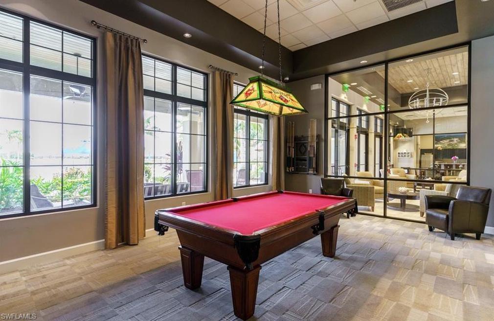 Game room featuring a billiard table with red felt, multiple large grid-patterned windows overlooking the pool and  lake, and a decorative stained-glass pendant light