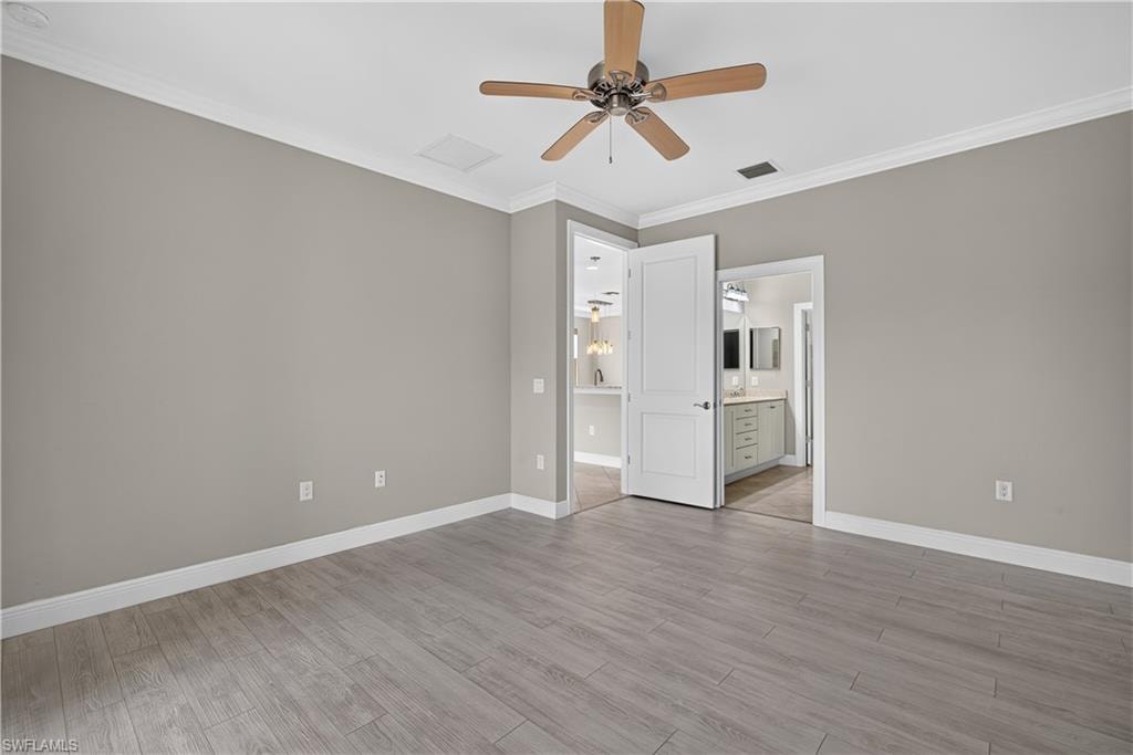 Spacious primary bedroom featuring wood-finish flooring, neutral wall tones, and crown molding