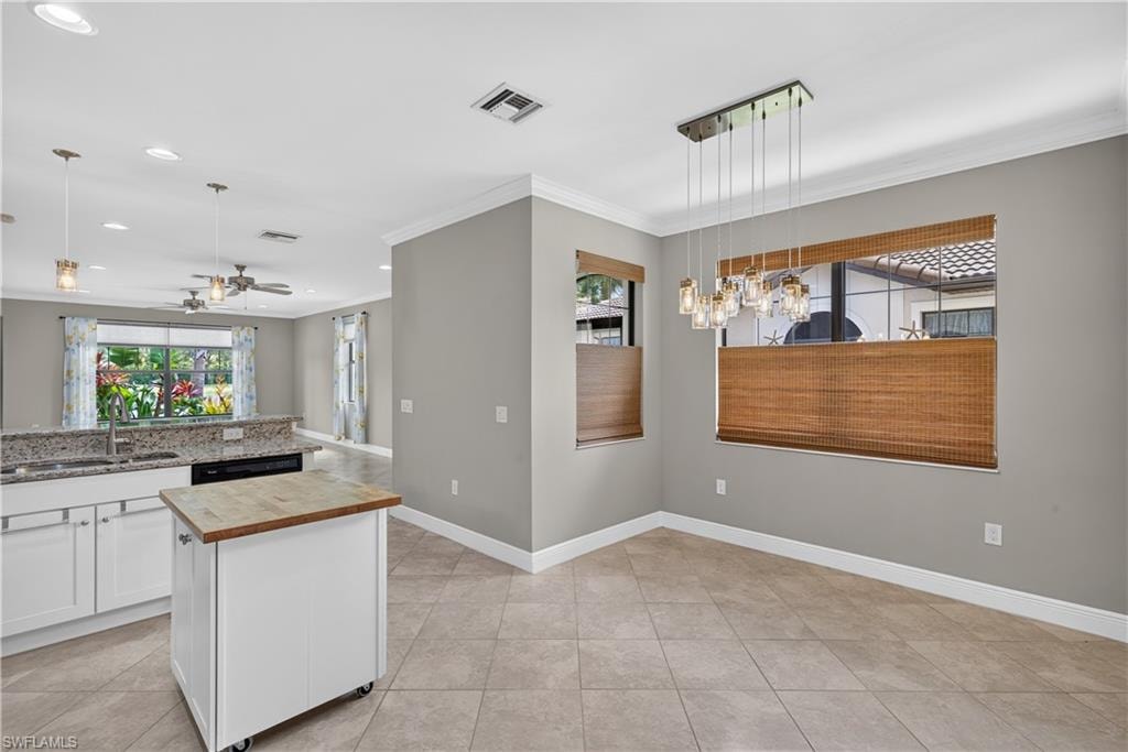 Dining area featuring a modern linear chandelier, tile flooring, and multiple windows with woven blinds that bring in a lot of natural light.