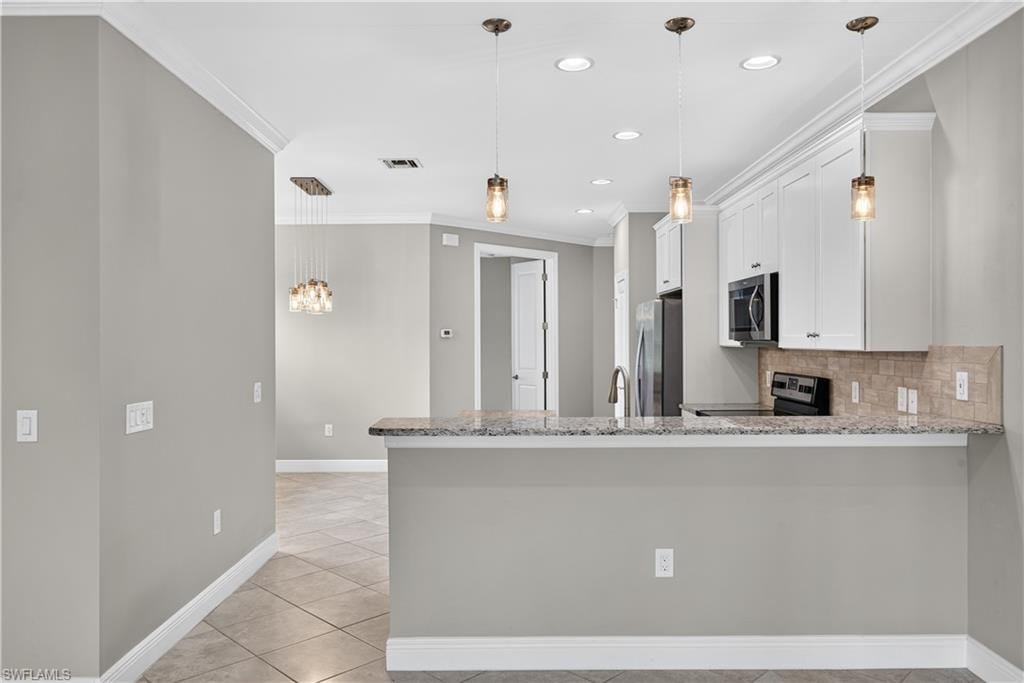 Kitchen featuring white shaker cabinetry, stainless steel appliances, a tiled backsplash and pendant lighting over the bar.