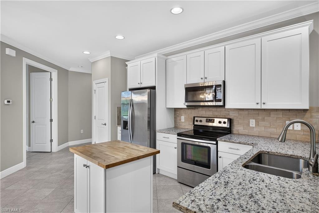 Kitchen featuring white cabinetry, stainless steel appliances, granite countertops, and a butcher block island