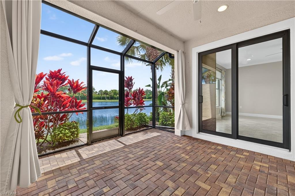 Screened lanai featuring brick paver flooring, a ceiling fan, recessed lighting, and sliding glass doors, with mature landscaping and water visible beyond