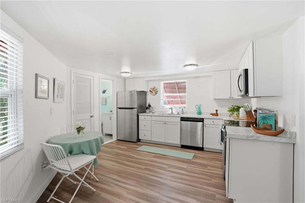 Bright kitchen with white cabinetry, wood-finish flooring, and stainless steel appliances - Virtually Edited Image
