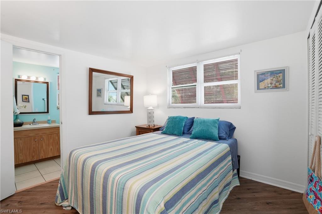 Bedroom featuring wood-finish flooring, white walls, and a double window with blinds - Virtually Edited Image