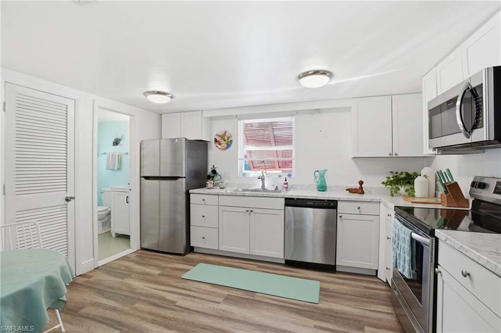 Kitchen featuring wood-finish flooring, white cabinetry, stainless steel appliances, and light-toned countertops - Virtually Edited Image