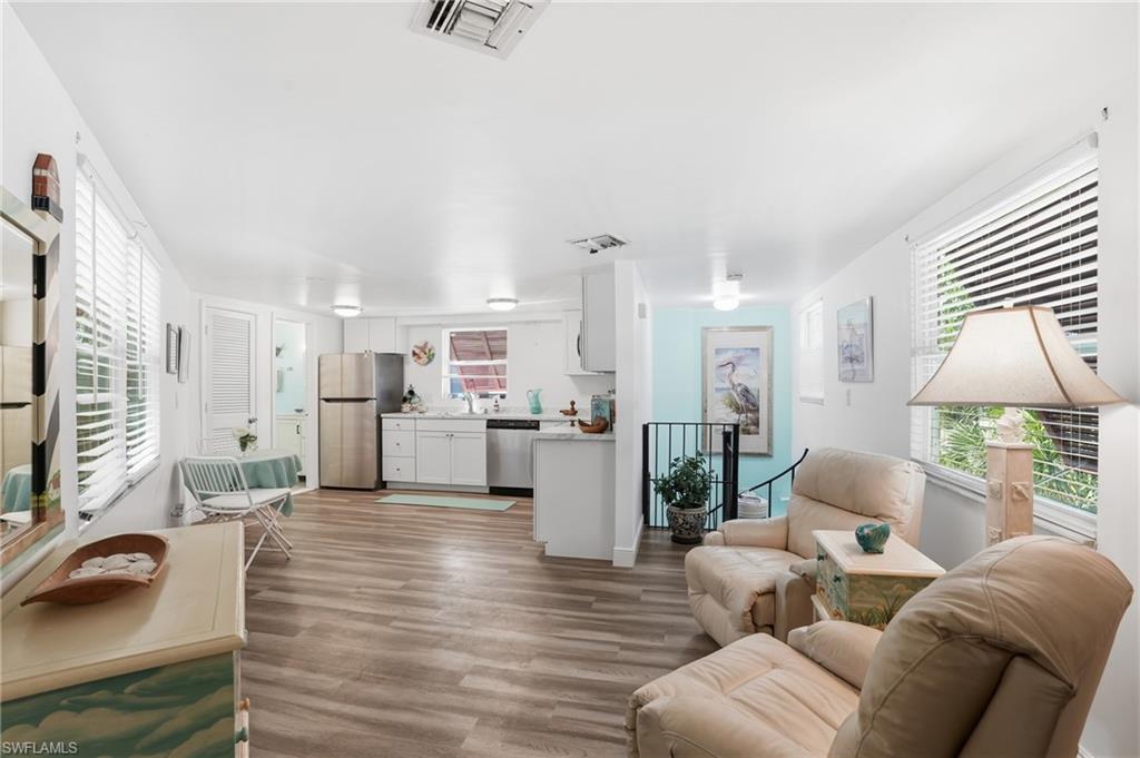 Open-concept living space with wood-finish flooring, white walls, and multiple windows with blinds - Virtually Edited Image