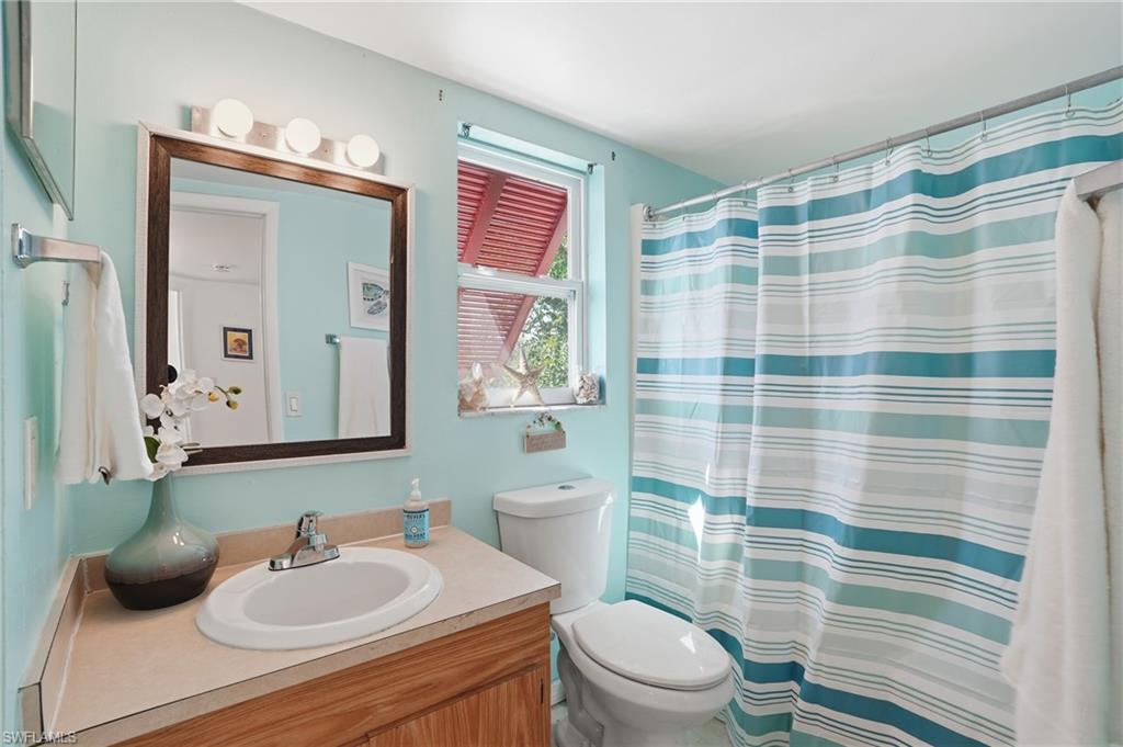 Bathroom featuring a wood-finish vanity with a built-in sink, a framed mirror, and a wall-mounted light fixture - Virtually Edited Image