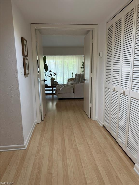 Open doorway leading to a brightly lit room with wood-finish flooring and white louvered closet doors