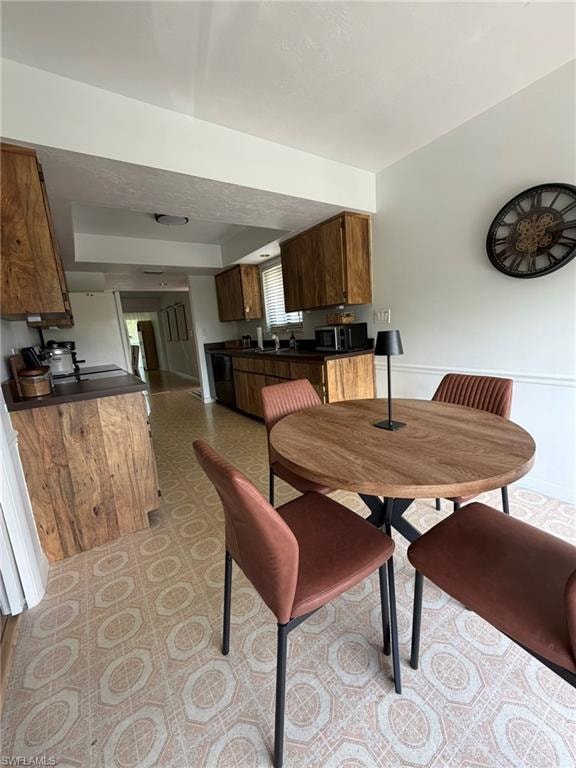Kitchen and dining area featuring wood-finish cabinetry, black countertops, and patterned floor tiling