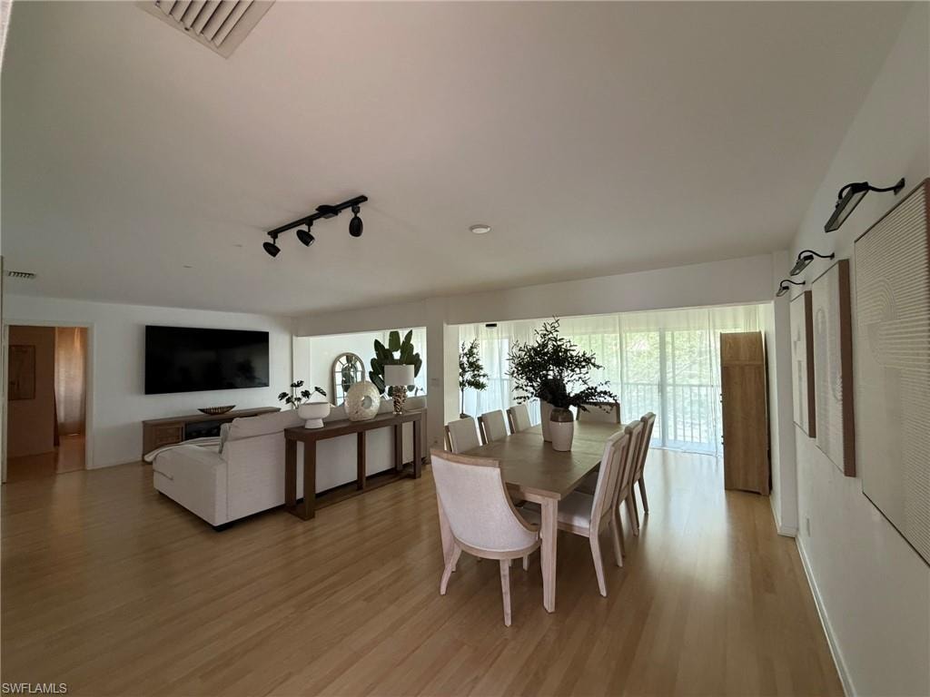 Open-concept living and dining area featuring light wood-finish flooring, white walls, and a sloped ceiling
