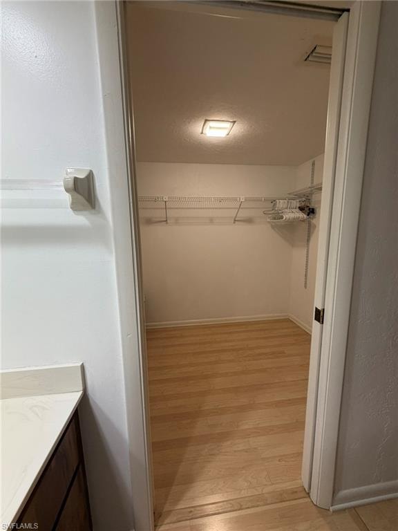 Walk-in closet featuring light wood-finish flooring, white walls, and built-in wire shelving