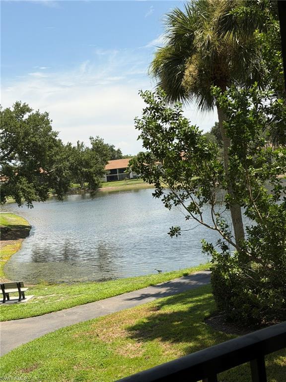 Tranquil water feature with a paved walking path, green lawn, and mature trees