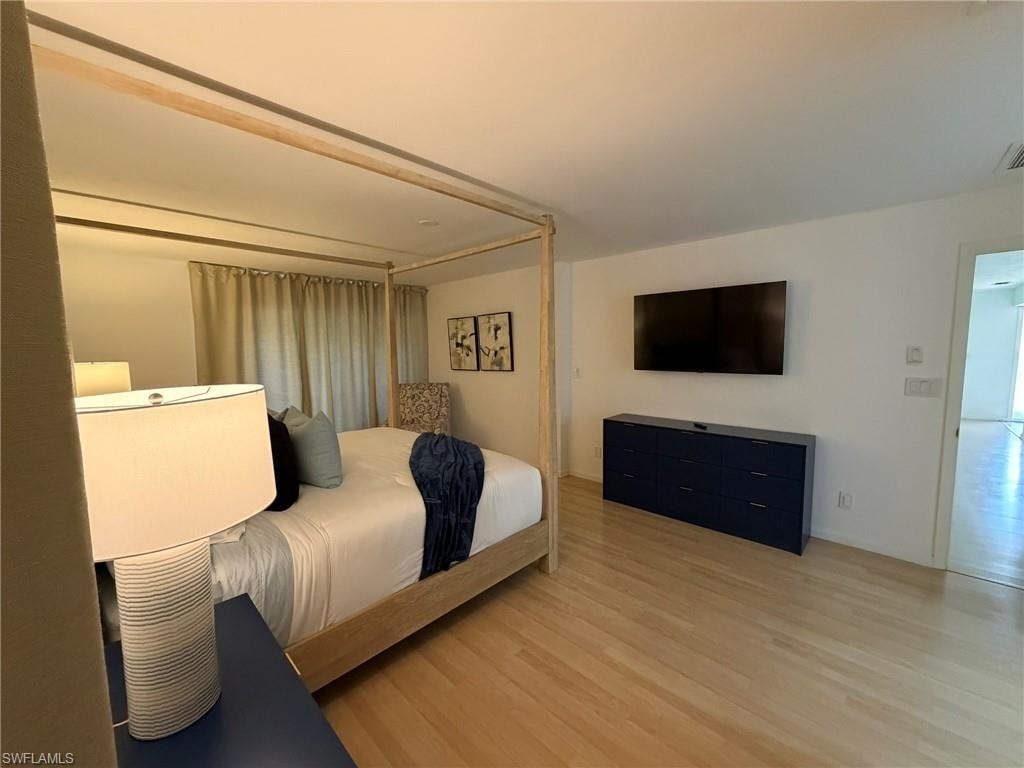 Spacious room featuring light wood-finish flooring, white walls, and a wall-mounted flat-screen display above a built-in dark blue cabinet
