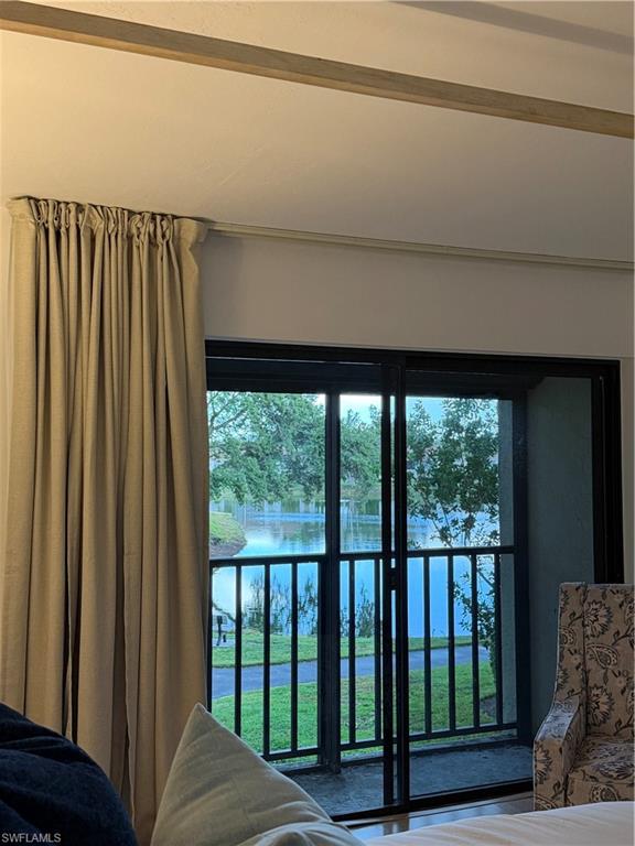 Sliding glass doors opening to a balcony with black railings overlooking a body of water and green landscaping