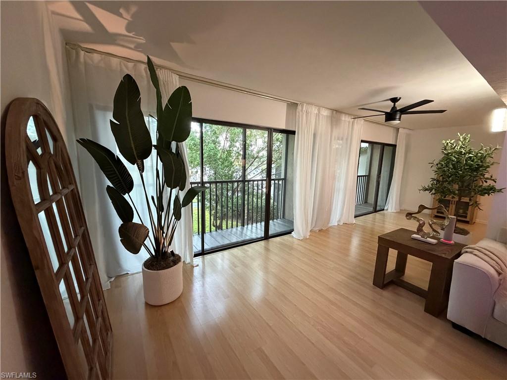 Light wood-finish flooring complemented by white walls, multiple floor-to-ceiling glass doors with direct balcony access, and a ceiling fan