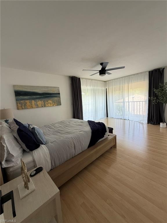 Bedroom featuring light wood-finish flooring, a contemporary ceiling fan, and expansive glass doors opening to a balcony with white railings
