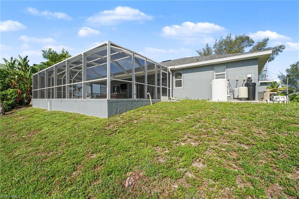 Rear exterior featuring a large screened enclosure, stucco siding, and a sloped grassy area