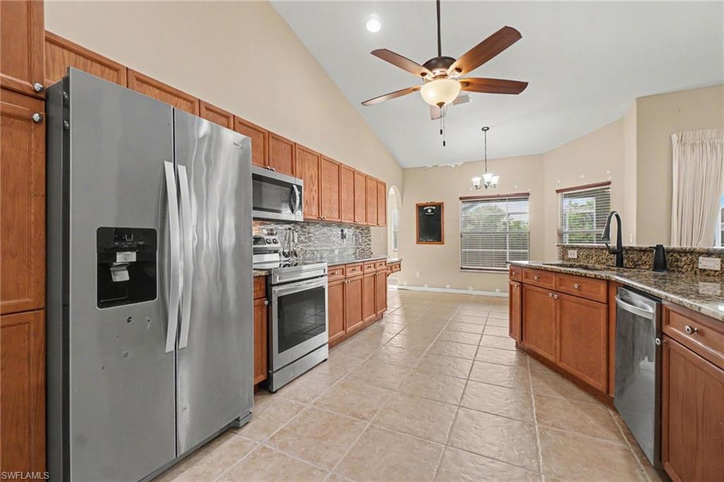 Kitchen featuring stainless steel appliances, wood-finish cabinetry, stone countertops, and tile flooring