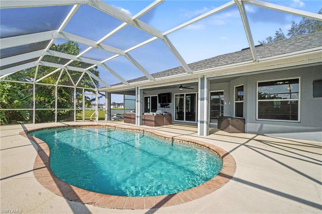 Screened enclosure featuring a freeform swimming pool with brick coping, an expansive concrete patio, and direct access to the interior via sliding glass doors